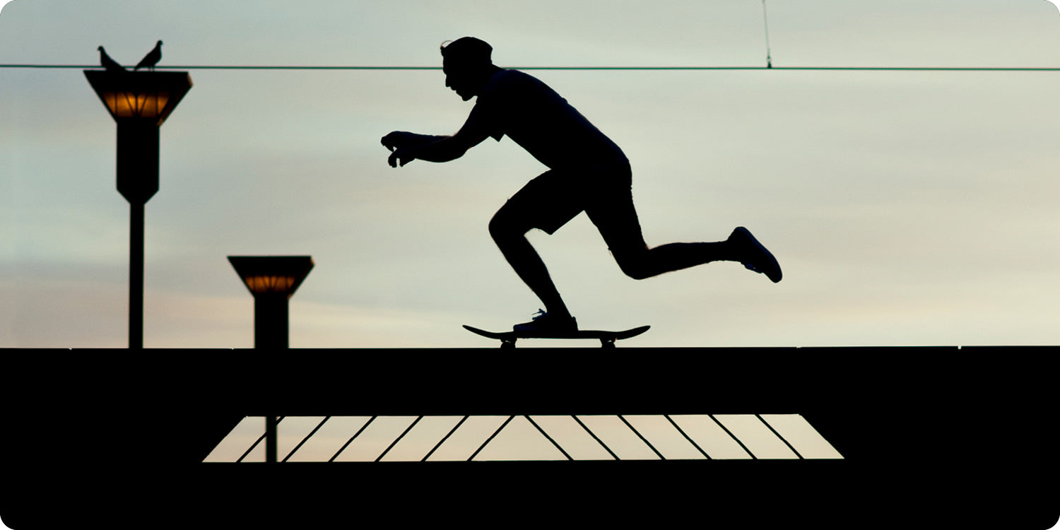 Silhouette of a person pushing on a skateboard on a flat surface.