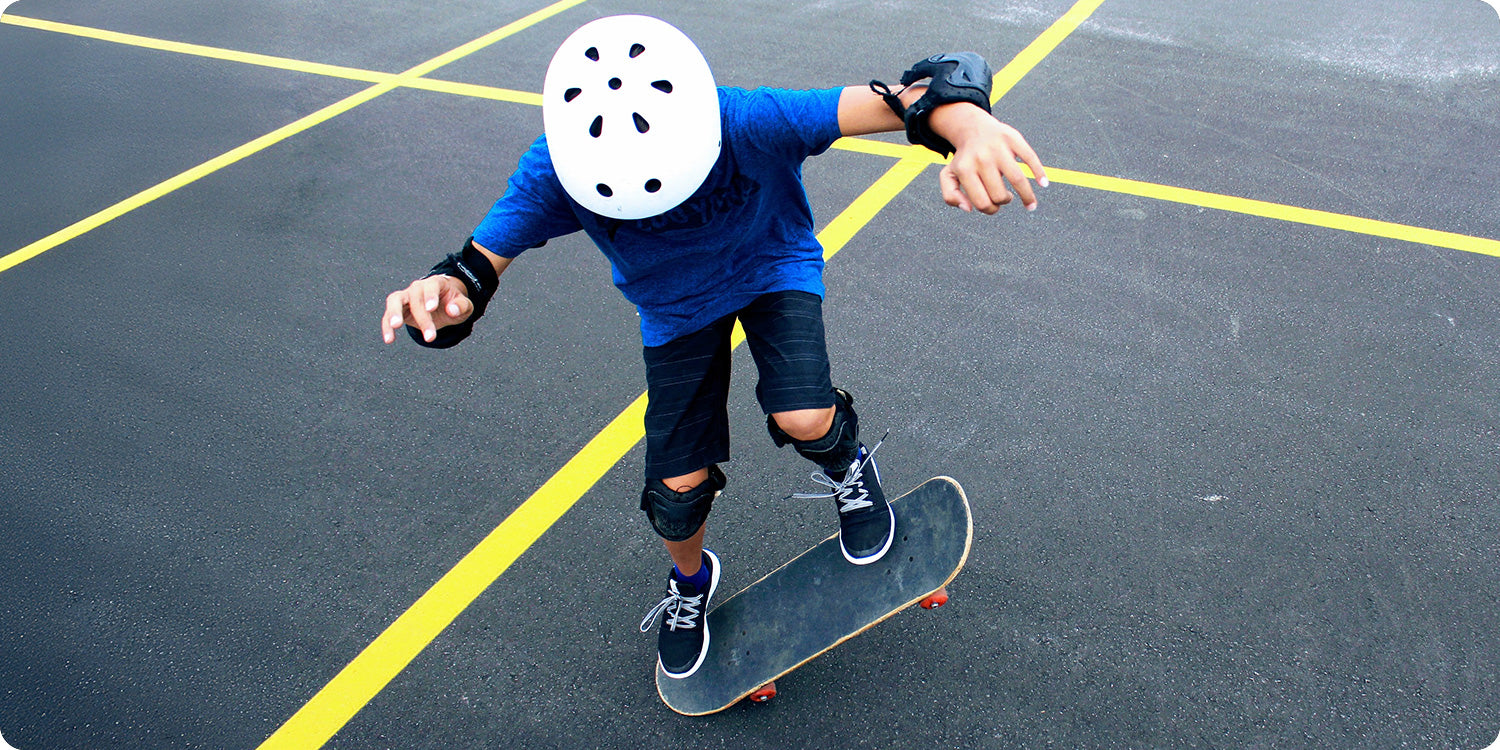 Photo of a younger person skateboarding on an asphalt surface while wearing protective gear.