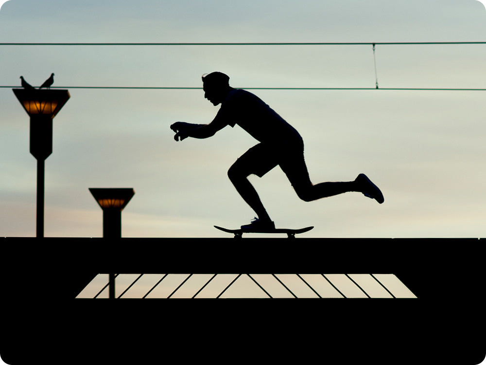 Silhouette of a person pushing on a skateboard on a flat surface.