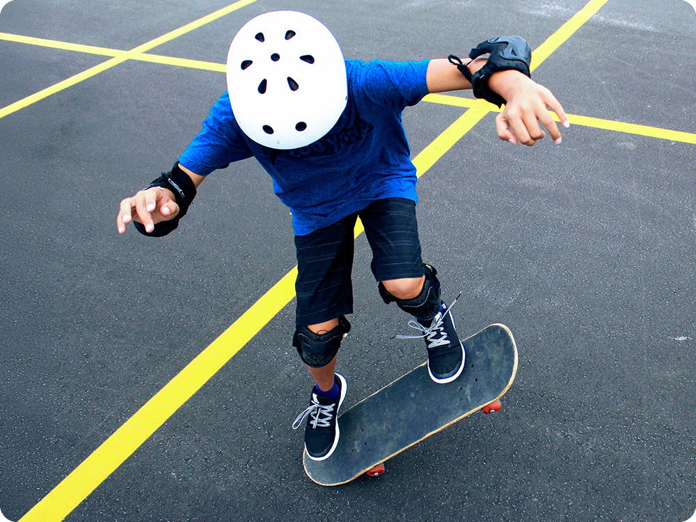 Photo of a younger person skateboarding on an asphalt surface while wearing protective gear.